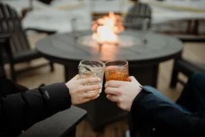 Two people clinking their glasses together by a fire