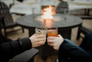 Two people clinking their glasses together by a fire
