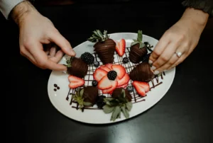 Person putting chocolate covered strawberries on a plate